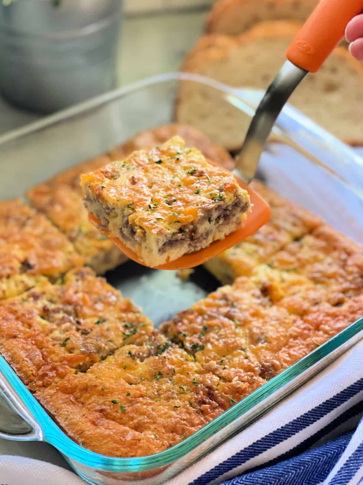 Glass square dish with egg caasserole and an orange spatula holding it over the dish.