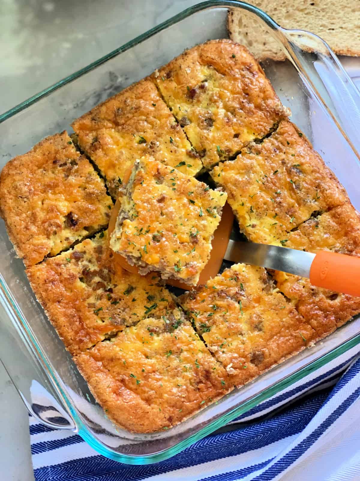 Glass square dish with 9 slices of egg with a spatuala pulling one out.