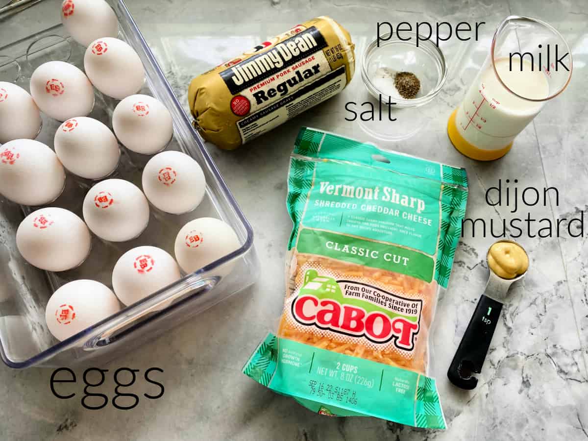 Ingredients on marble countertop: eggs, sausage, cheese, salt, peppr, milk, and djion mustard.