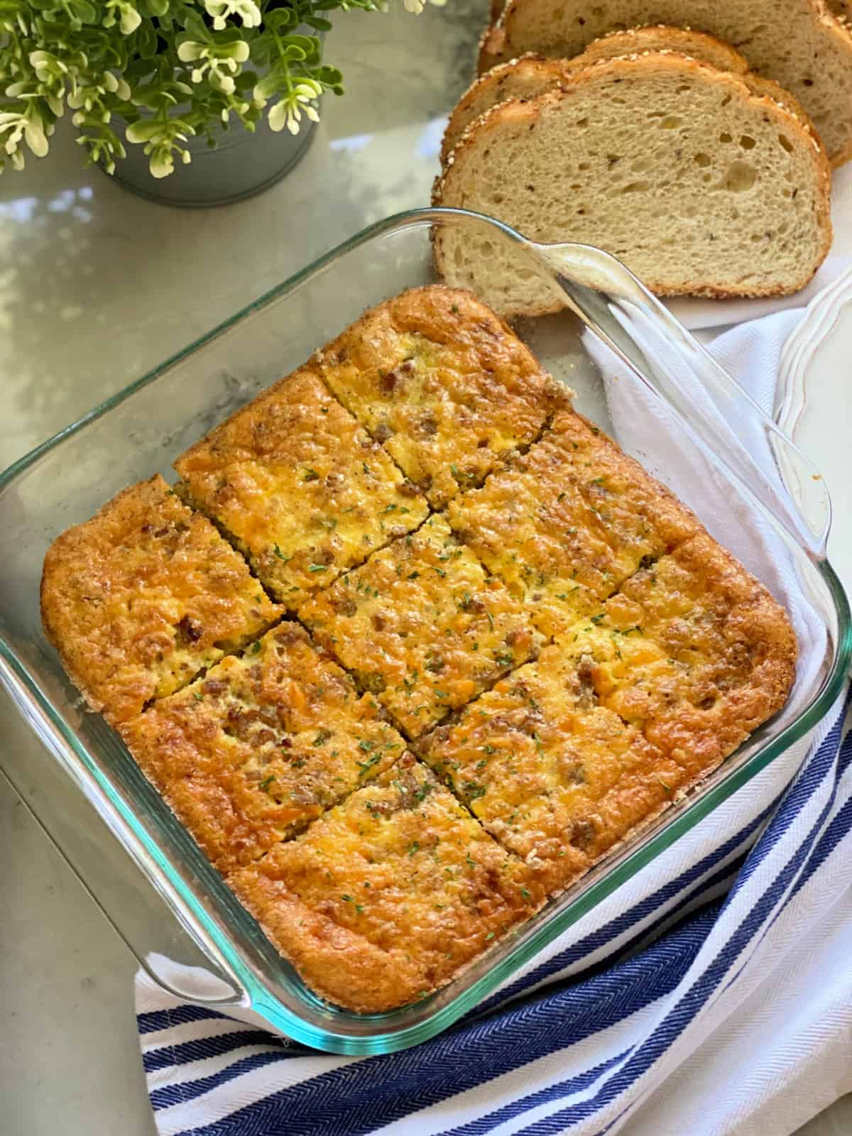 Glass square dish with egg casserole cut into 9 squares with bread slices on the side.