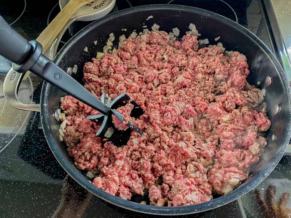Raw ground beef and pork in a skillet with onions and a meat grinder stick.