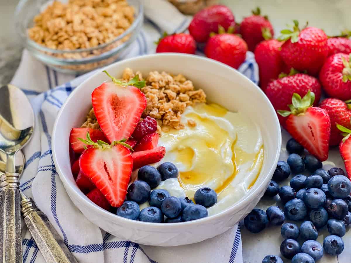 White bowl filled with yogurt, honey, bleuberries, strawberries, and granola.