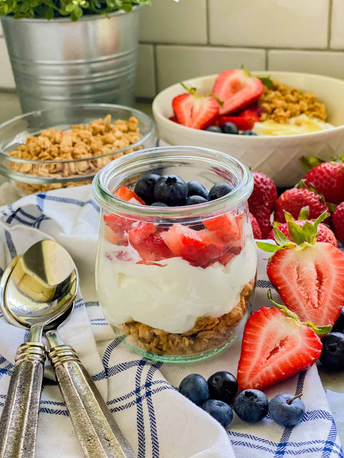 Glass jar filled with granola, yogurt, and fruit with spoons next to it.