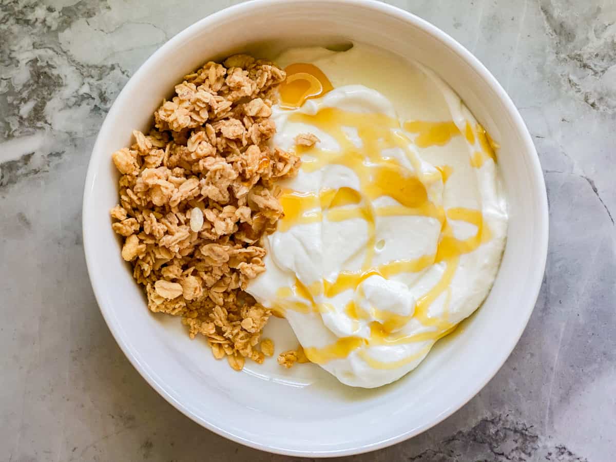 White bowl filled with yogurt, honey, and granola on marble countertop.