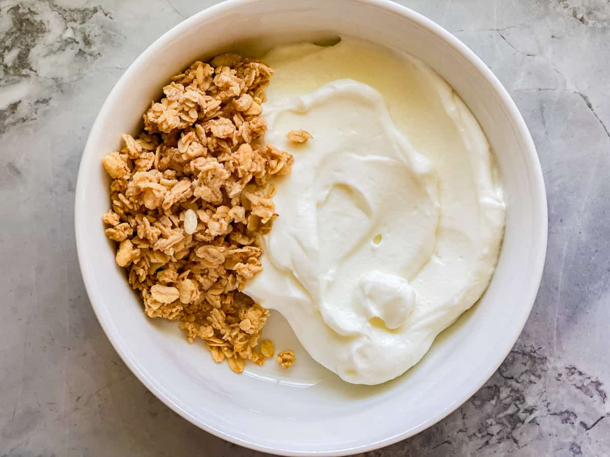 White bowl filled with yogurt and granola on marble countertop.