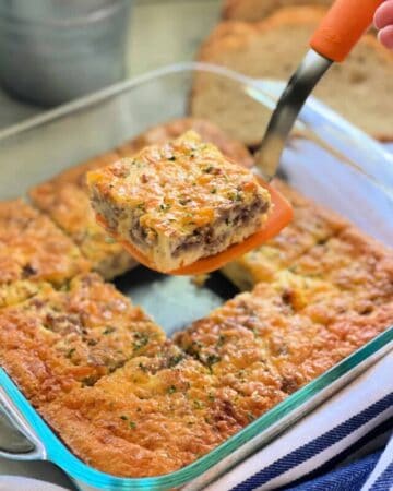 Glass square dish with egg caasserole and an orange spatula holding it over the dish.