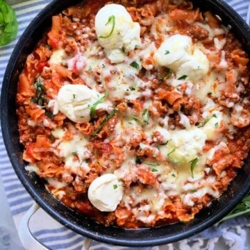 Black saute pan with lasagana cooked inside resting on a striped cloth.