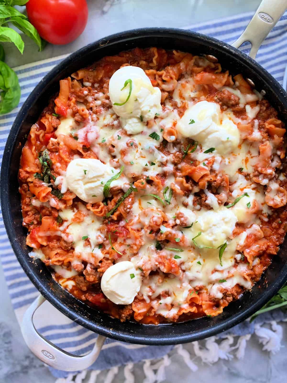 Black saute pan with lasagana cooked inside resting on a striped cloth.