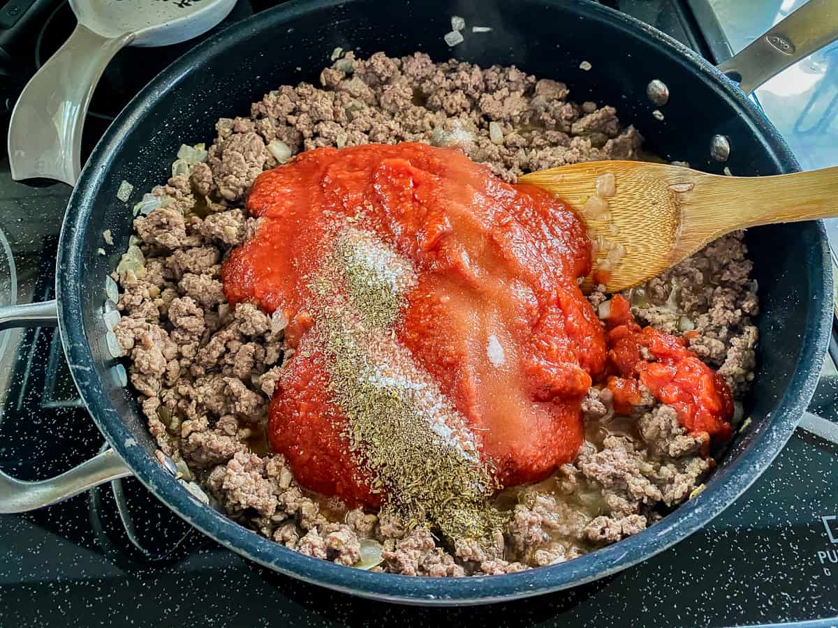 Cooked ground beef with sauce and spices on top in a black skillet on the stove top.