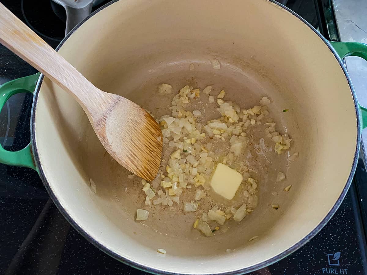 White pot with a wooden spoon with onions, garlic and butter.