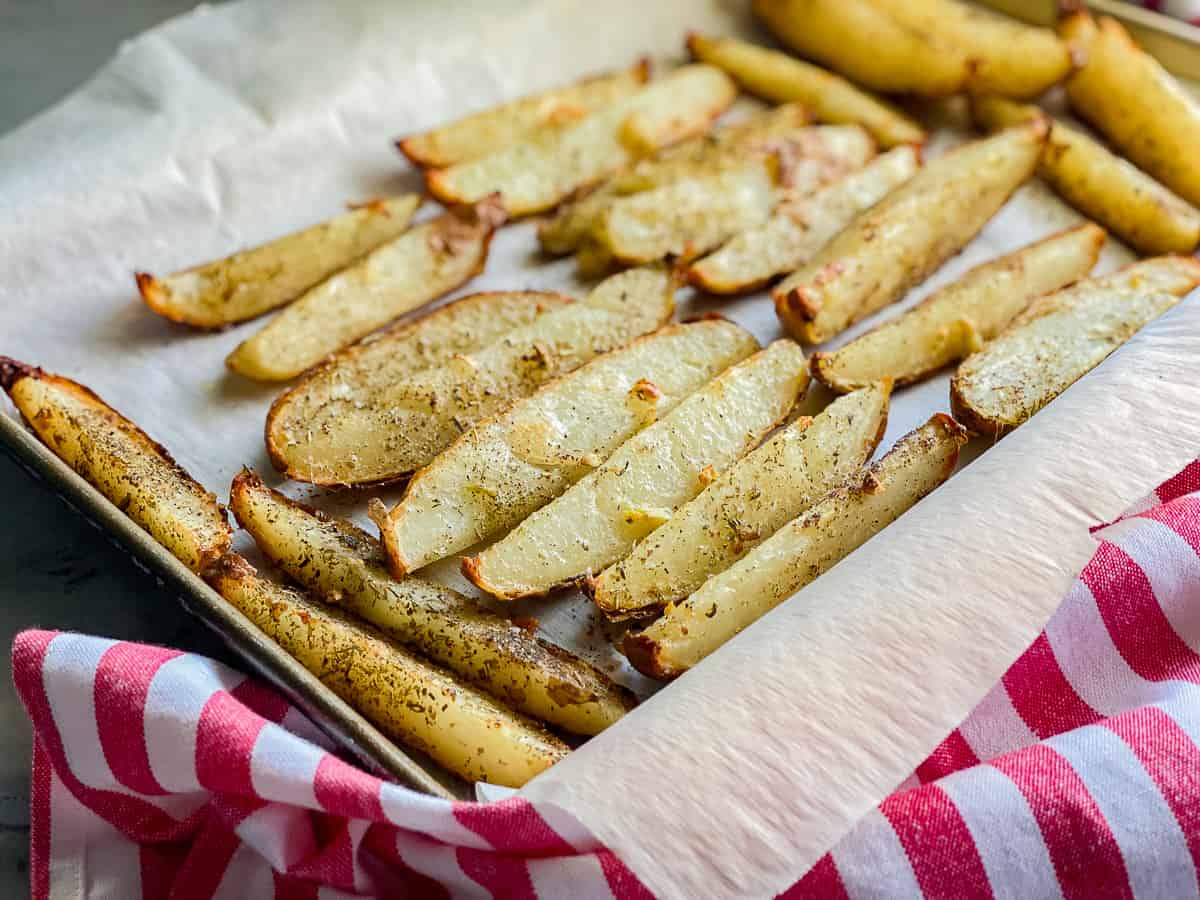Baking sheet lined with white parchment paper with potato wedges.