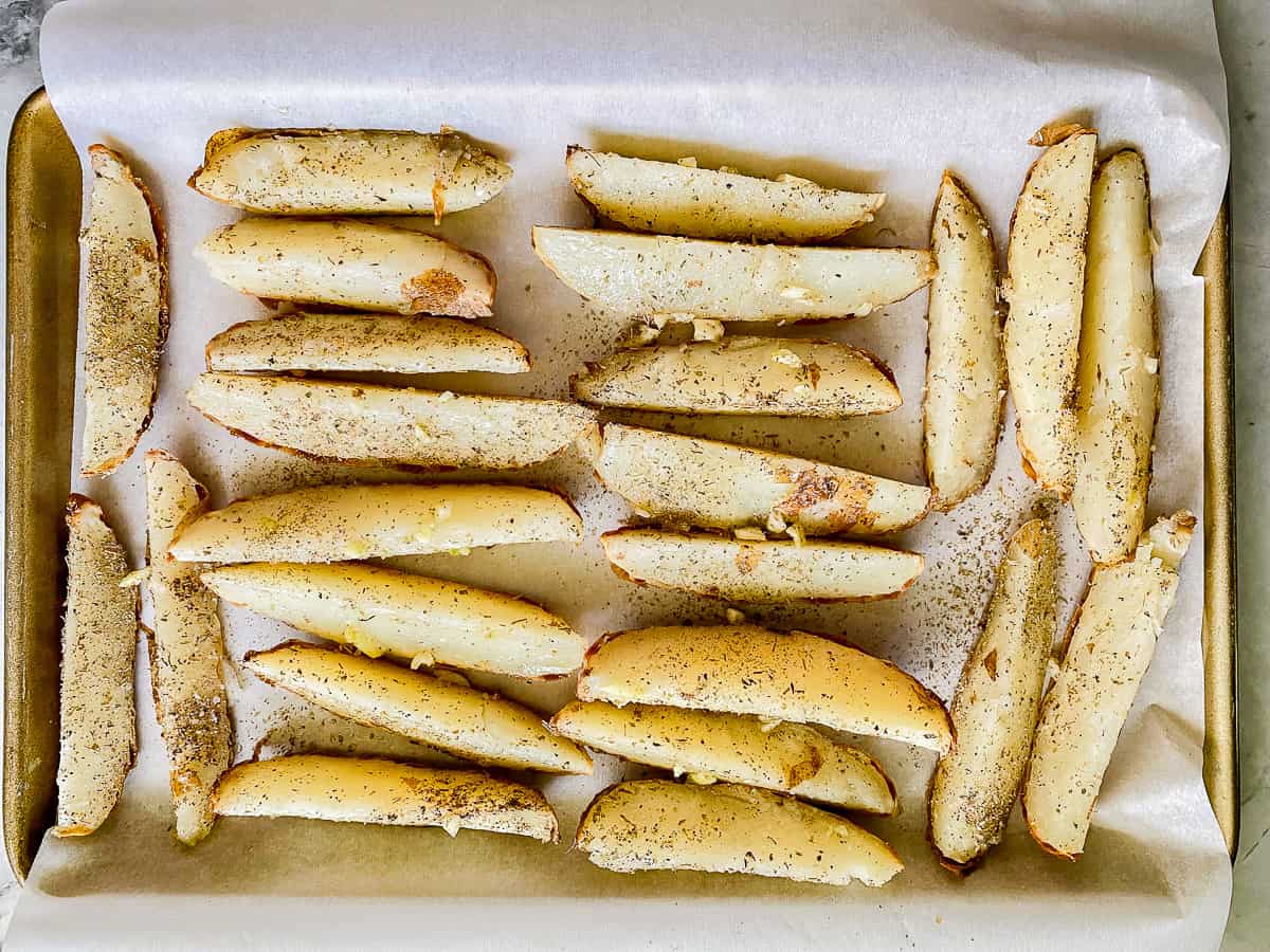 Baking tray lined with parchment paper and potato wedges.