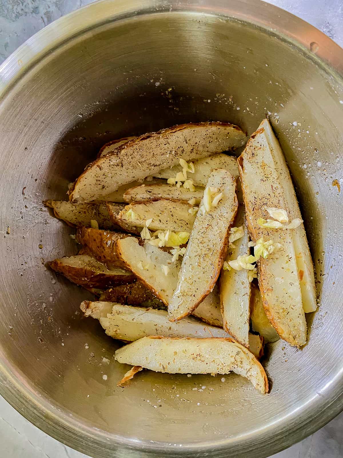 Silver bowl with potato slices and seasoning.