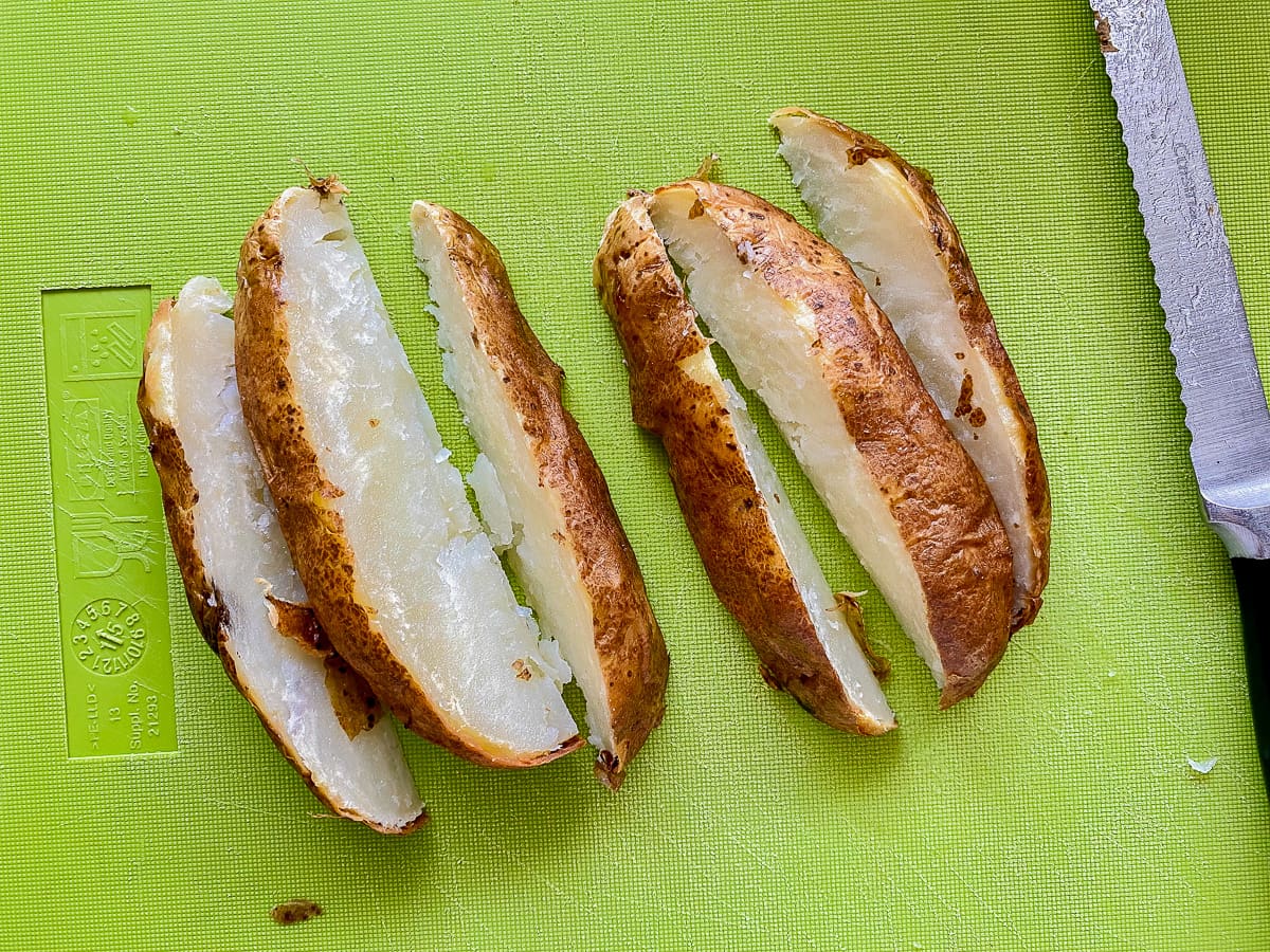 Green cutting board with serrated knife with 6 slices of potatoes.