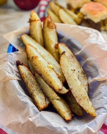Blue basket with parchment paper and potato wedges in it.