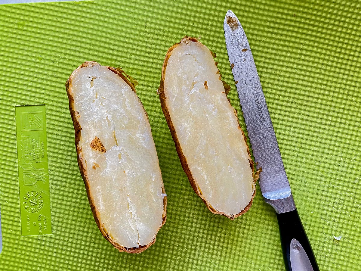 Green cutting board with a baked potato cut in half with a serated knife next to it.