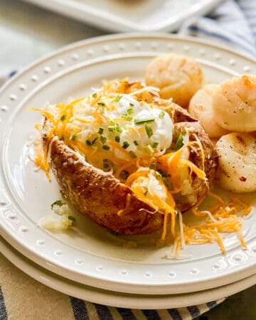 Two white plates stacked with a loaded baked potato and scallops.