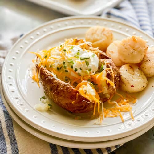 Two white plates stacked with a loaded baked potato and scallops.