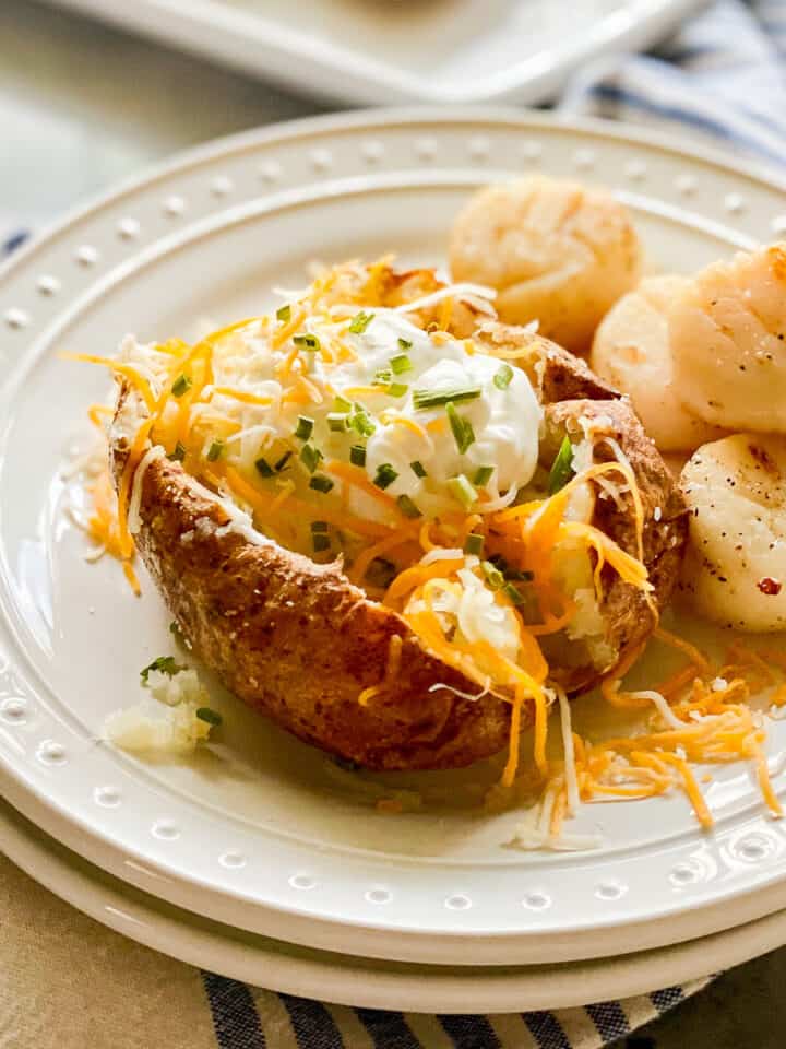 Two white plates stacked with a loaded baked potato and scallops.