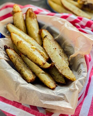 Basket filled with potato wedges on a red and white striped cloth.