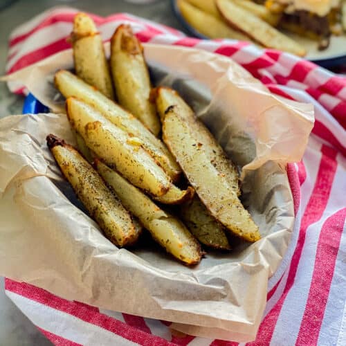 Basket filled with potato wedges on a red and white striped cloth.