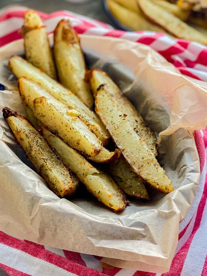 Basket filled with potato wedges on a red and white striped cloth.