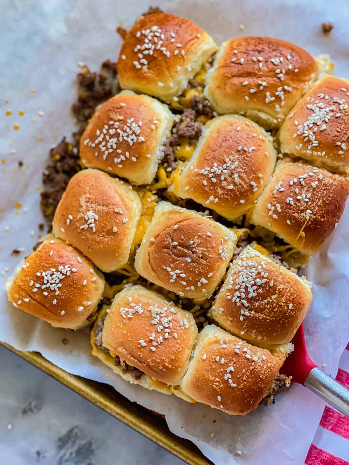 12 cut ground beef and cheese sliderss on a parchment lined baking sheet with a red spatula.