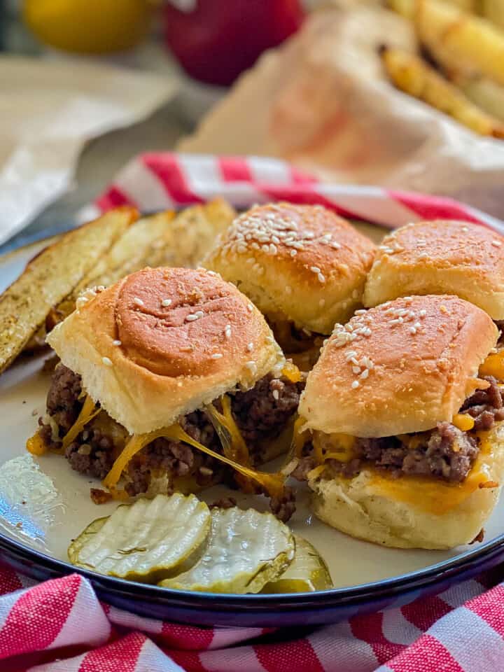 White plate filled with 4 sliders with pickles resting on a red and white striped napkin.