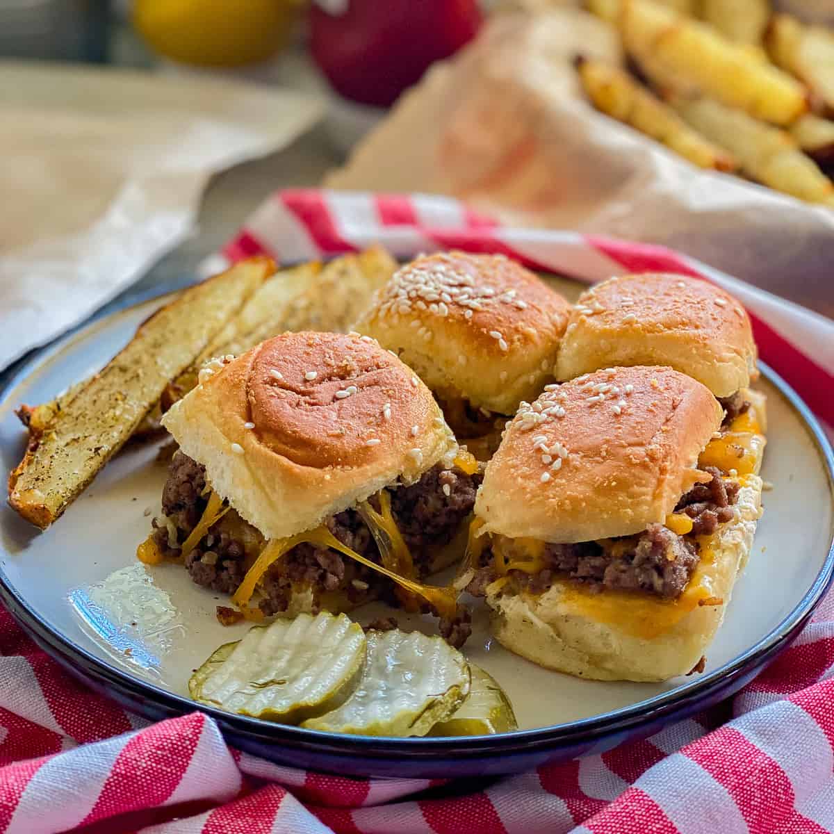 White plate filled with 4 sliders with pickles resting on a red and white striped napkin.