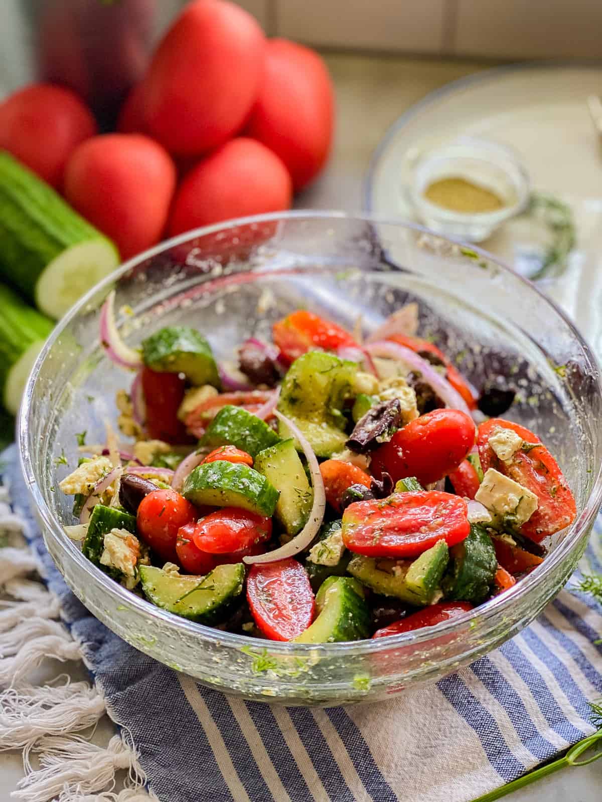 Glass bowl filled with sliced tomatoes, cucumbers, onions, and chunkss of feta.