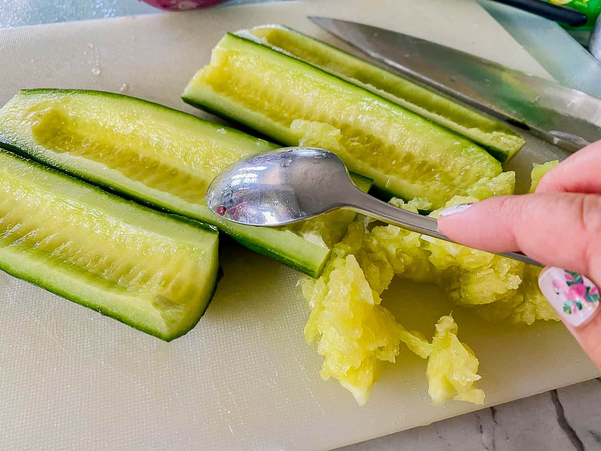 Female hand scraping sseeds from a sliced opened cucumber.