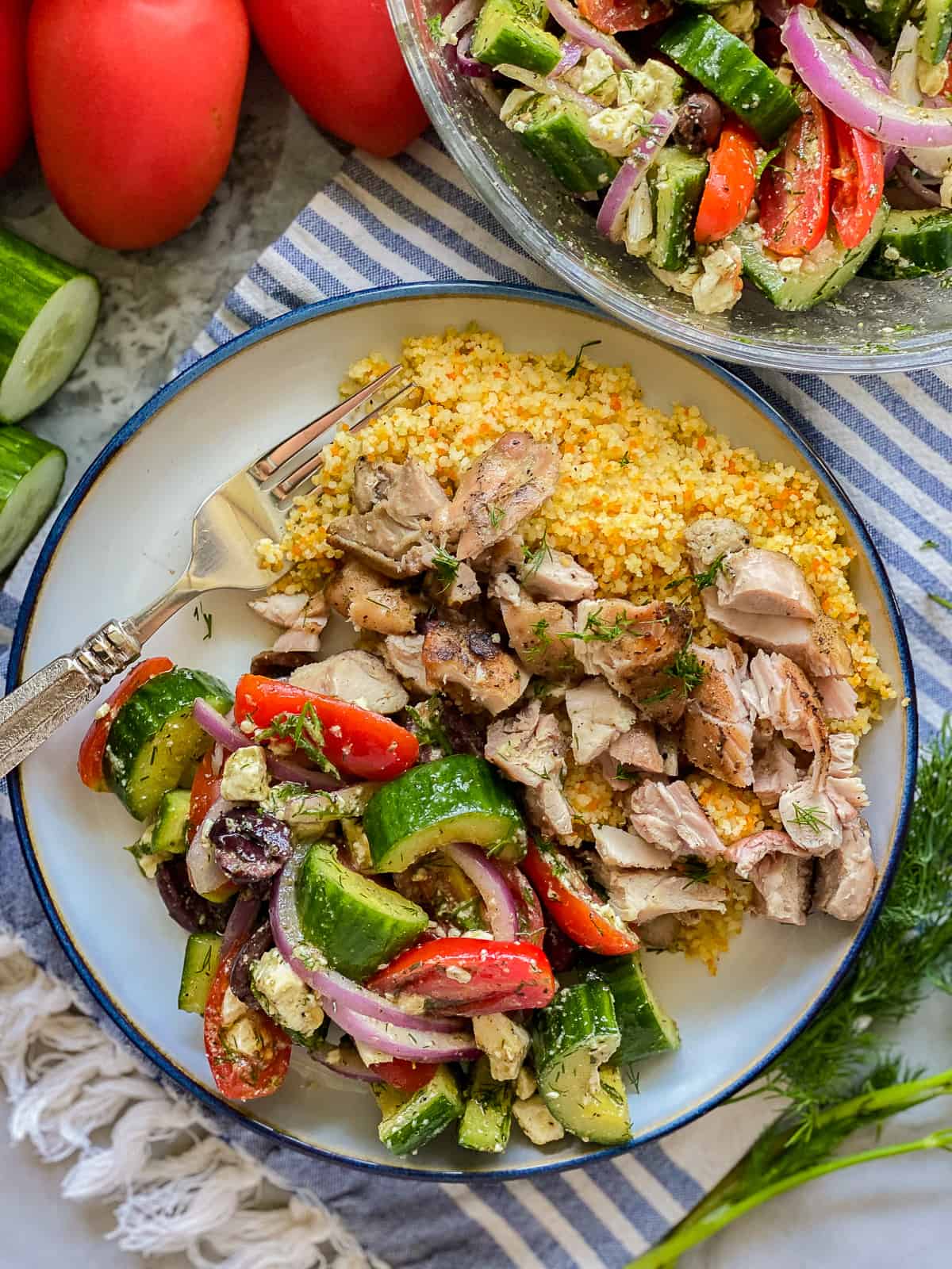 White plate with blue rim filled with cucumber salad, chiken and couscous with fork on plate.