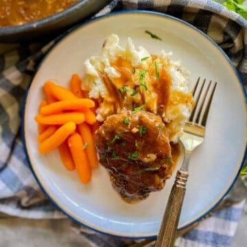 White plate filled with beef patty, mashed potatoes, and carrots.