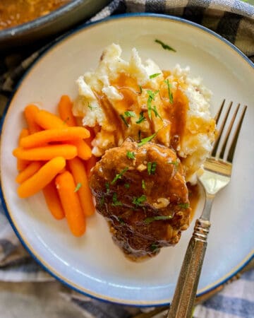 White plate filled with beef patty, mashed potatoes, and carrots.