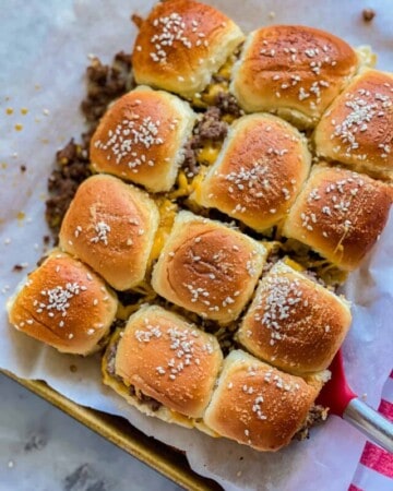 12 cut ground beef and cheese sliderss on a parchment lined baking sheet with a red spatula.