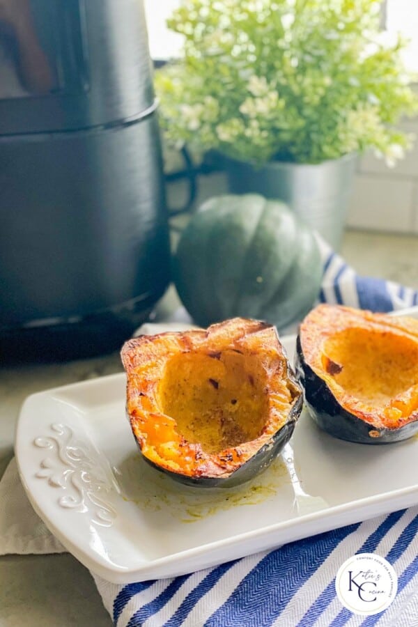 Two acorn squash cooked pieces on a white platter with a logo on the bottom right corner.