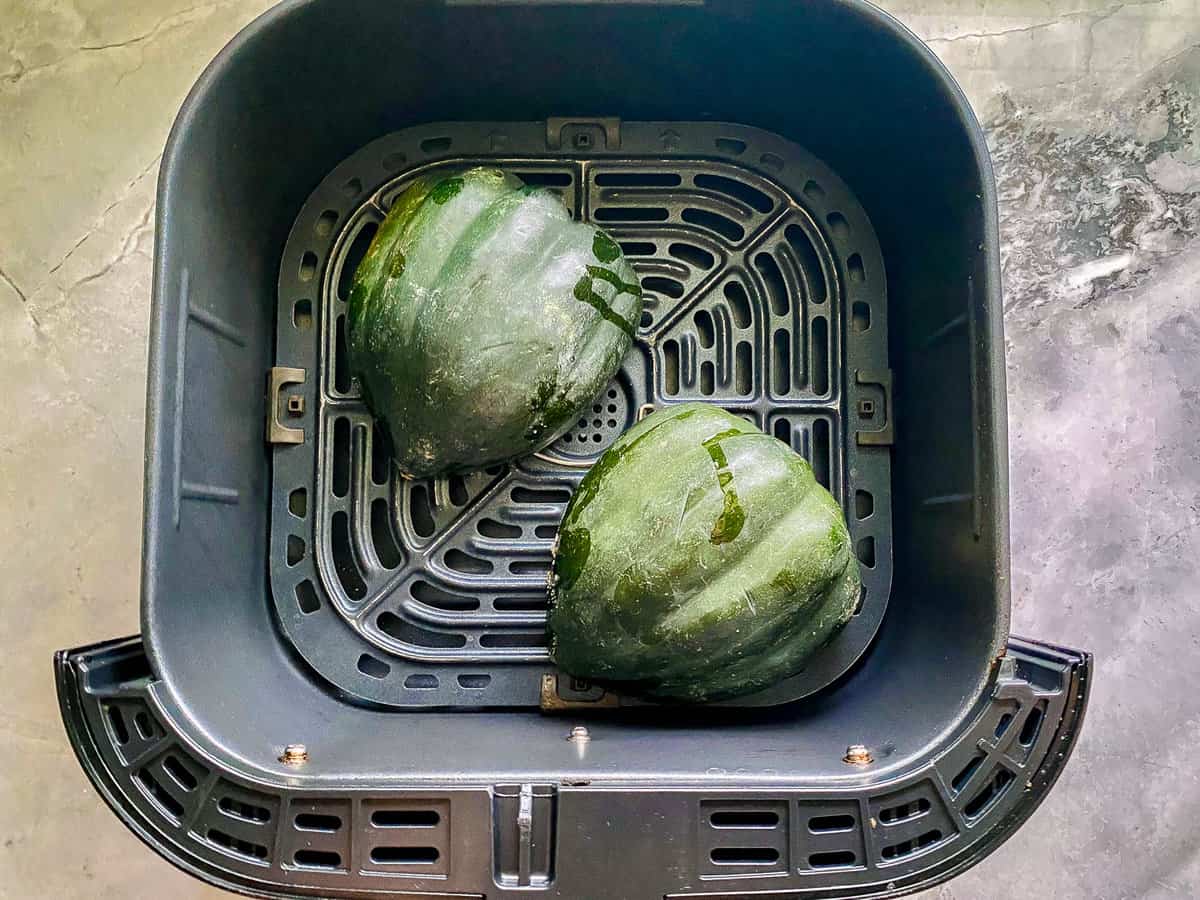 Air fryer basket with acorn squash face down.