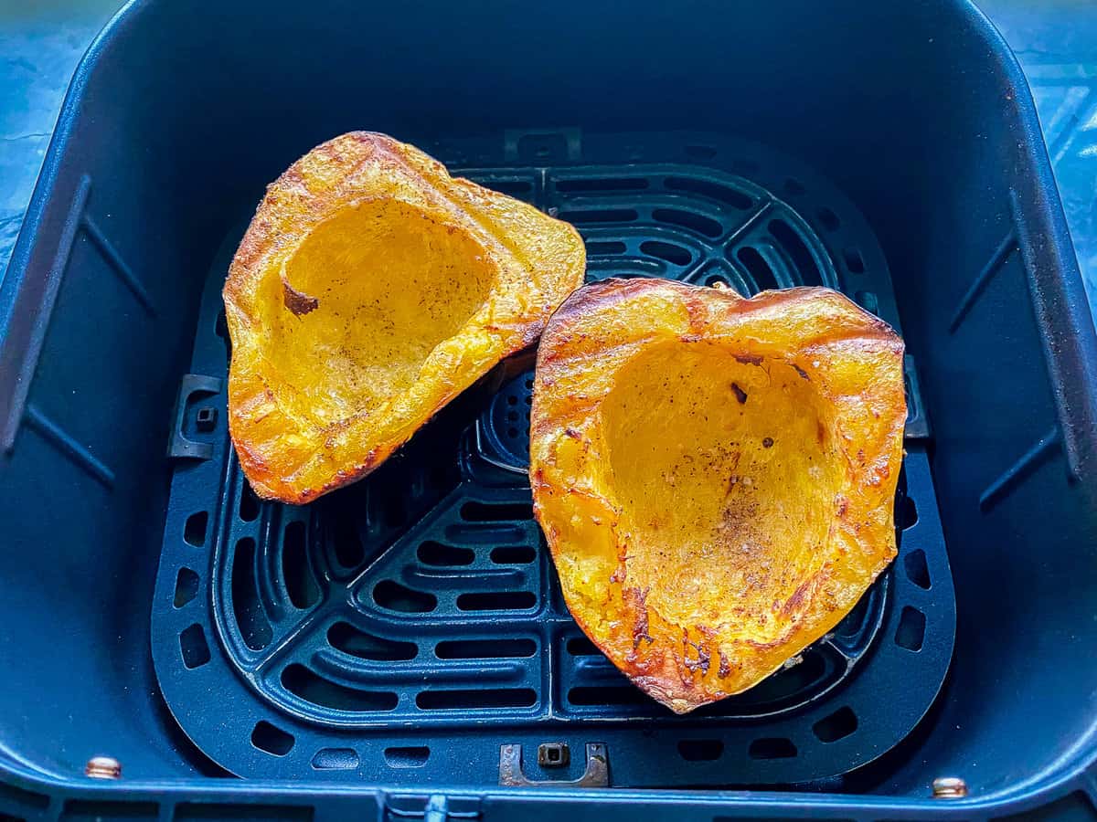 Air fryer basket with two pieces of acorn squash cooked.