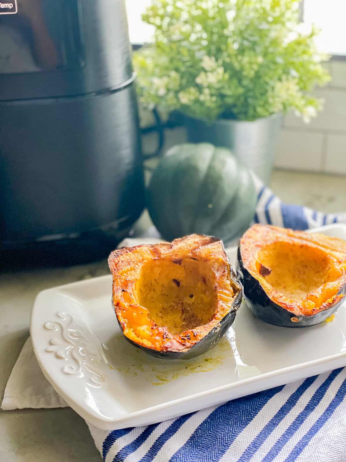 White platter with two cooked acorn squash with air fryer in background.