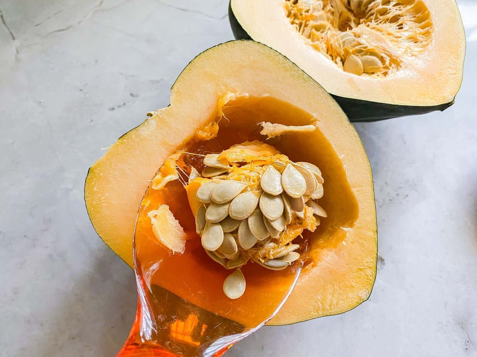 Orange scoop, scooping out seeds from the middle of a cut acorn squash.