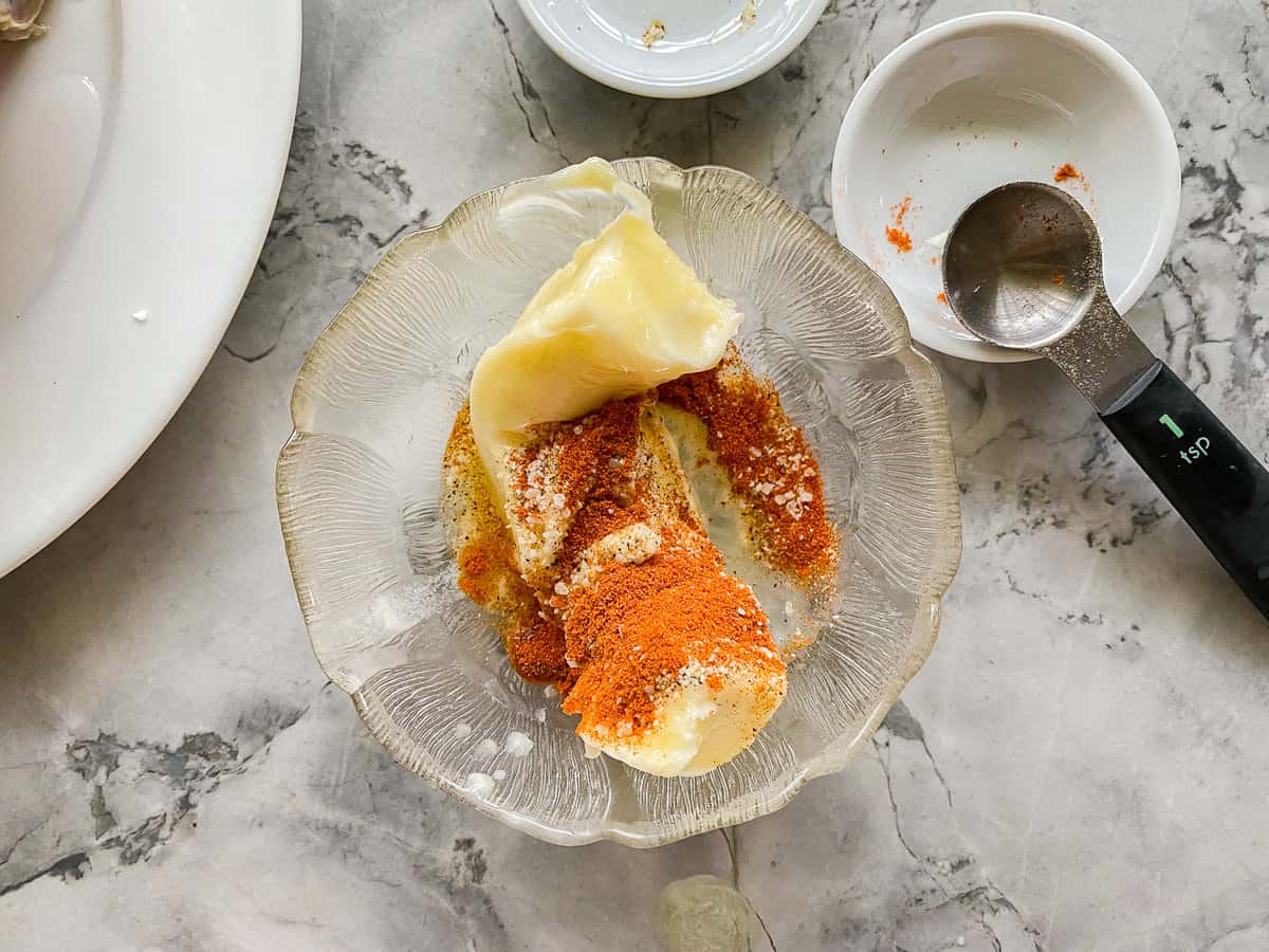 Glass bowl filled with butter and seasonings on a marble countertop.