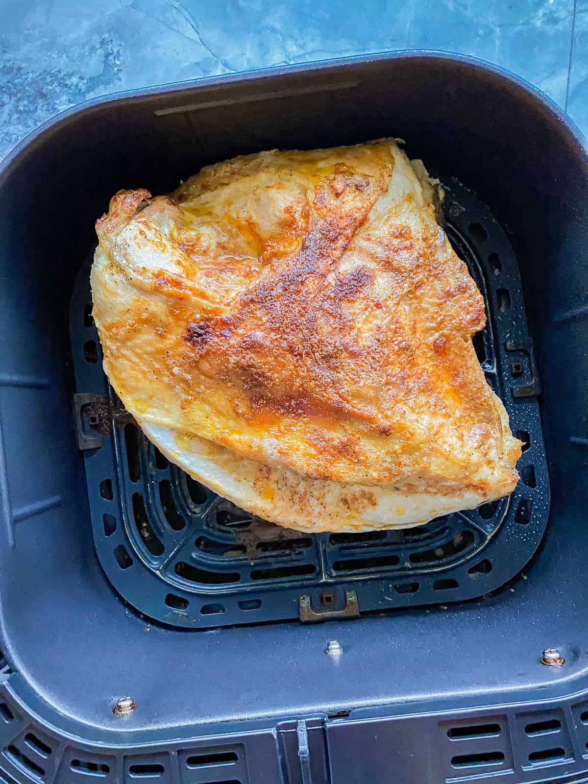 Black air fryer basket with a turkey that is half cooked in basket.