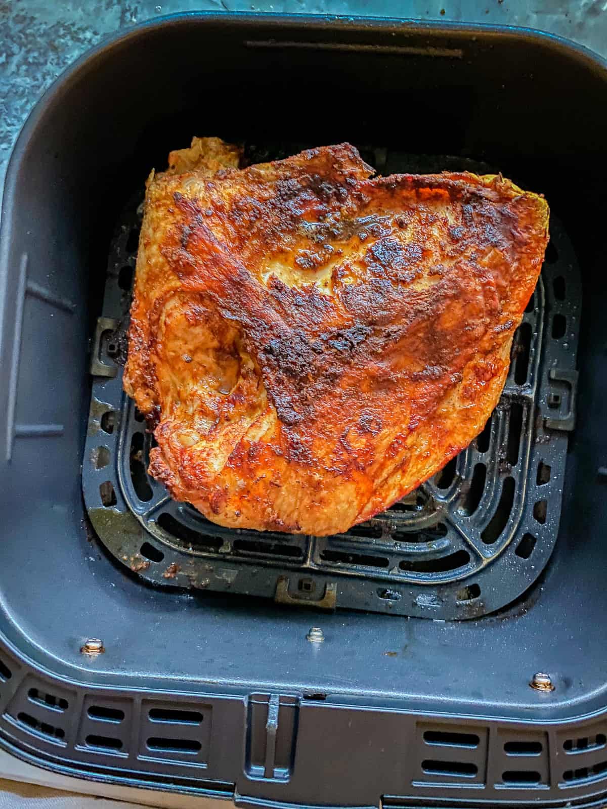 Black air fryer basket filled with a cooked half turkey breast.