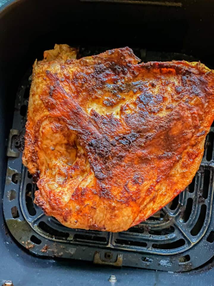 Cooked seasoned turkey breast in a black air fryer basket.