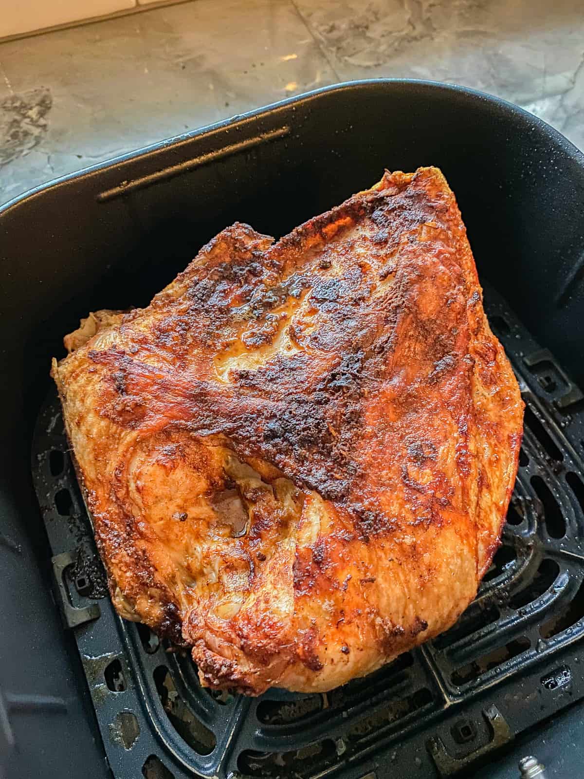 Cooked half turkey breast in an Air Fryer basket.
