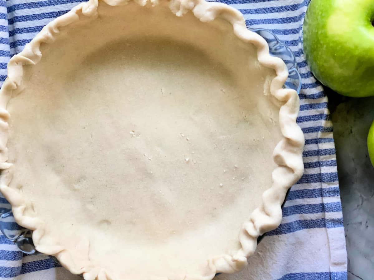 Raw pie crust in a glass pie plate on top of a white and blue striped cloth.