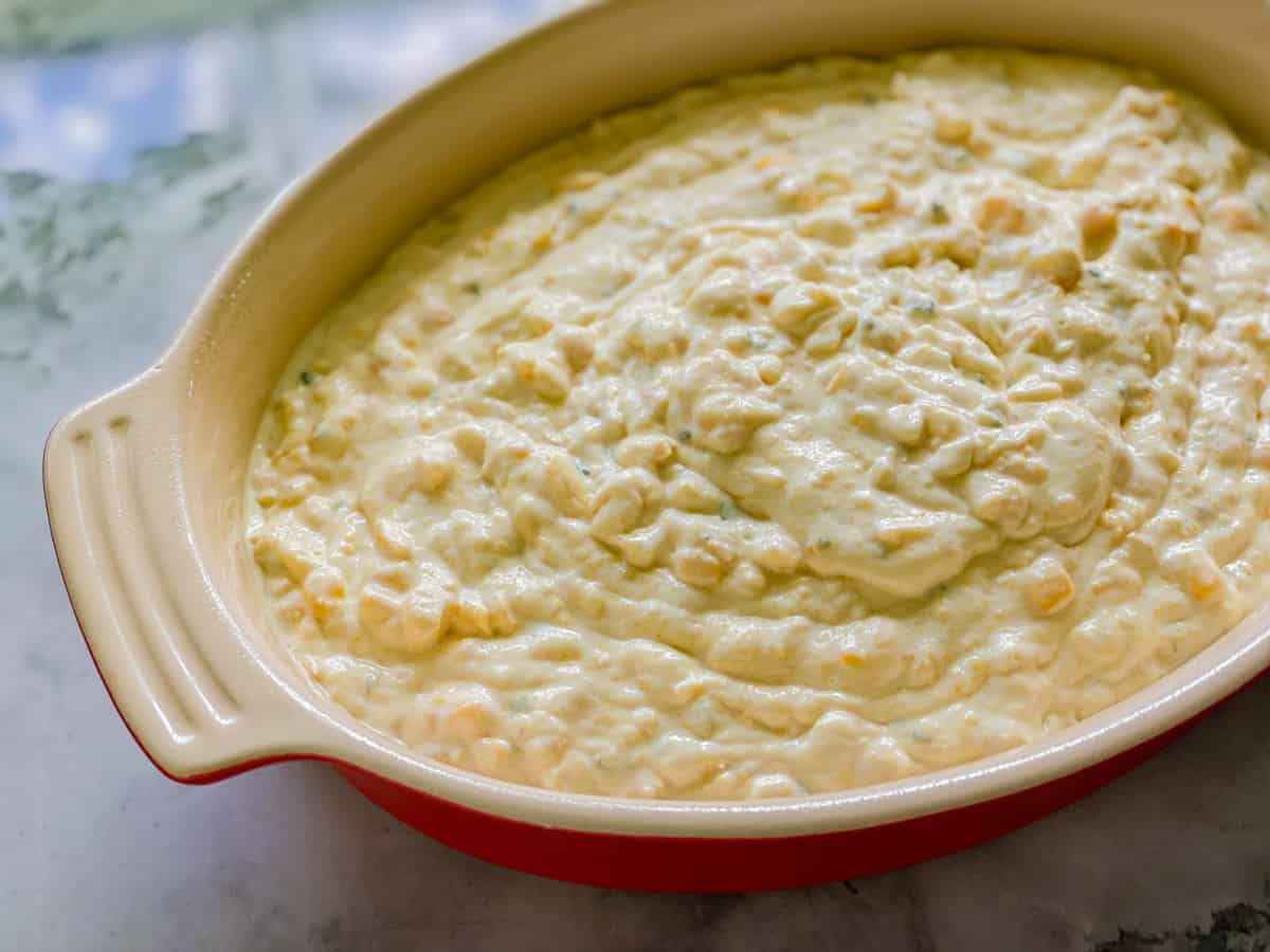 Oval baking dish filled with raw corn casserole on a marble countertop.