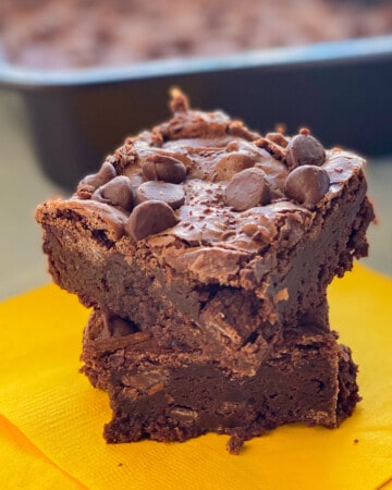 Two brownies stacked on top of each other sitting on a yellow napkin.