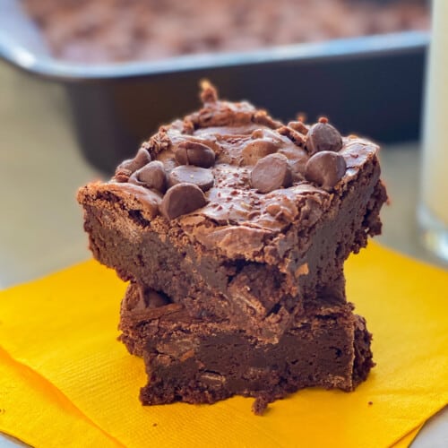 Two brownies stacked on top of each other sitting on a yellow napkin.