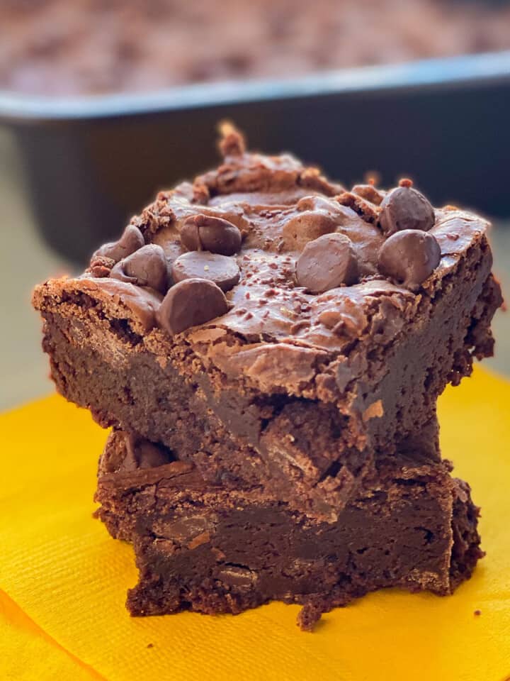 Two brownies stacked on top of each other sitting on a yellow napkin.